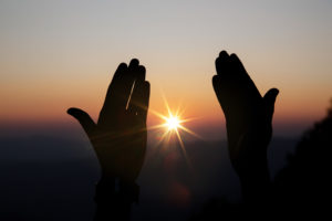 Zwei zum Gebet ausgebreitete Hände, dazwischen scheint die Sonne hindurch